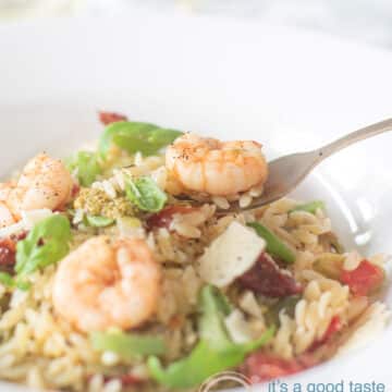 part of a white deep plate filled with pesto orzo with Parmesan, shrimp, string beans. A fork is taking a bite