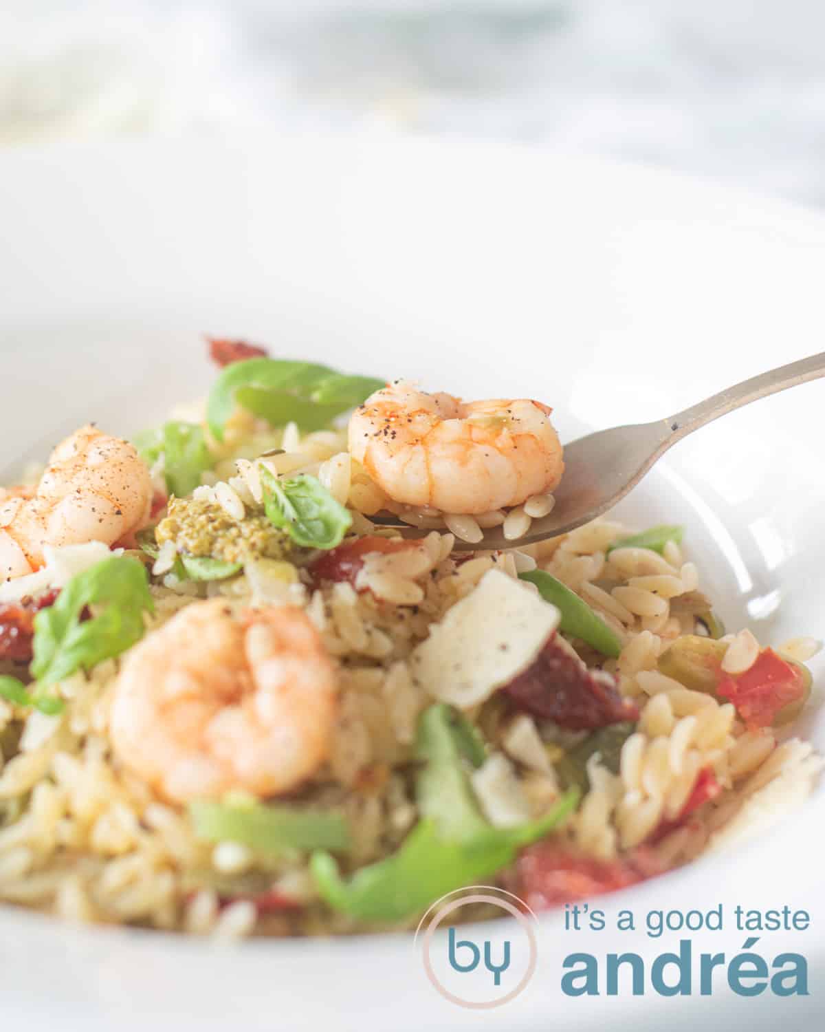 part of a white deep plate filled with pesto orzo with Parmesan, shrimp, string beans. A fork is taking a bite