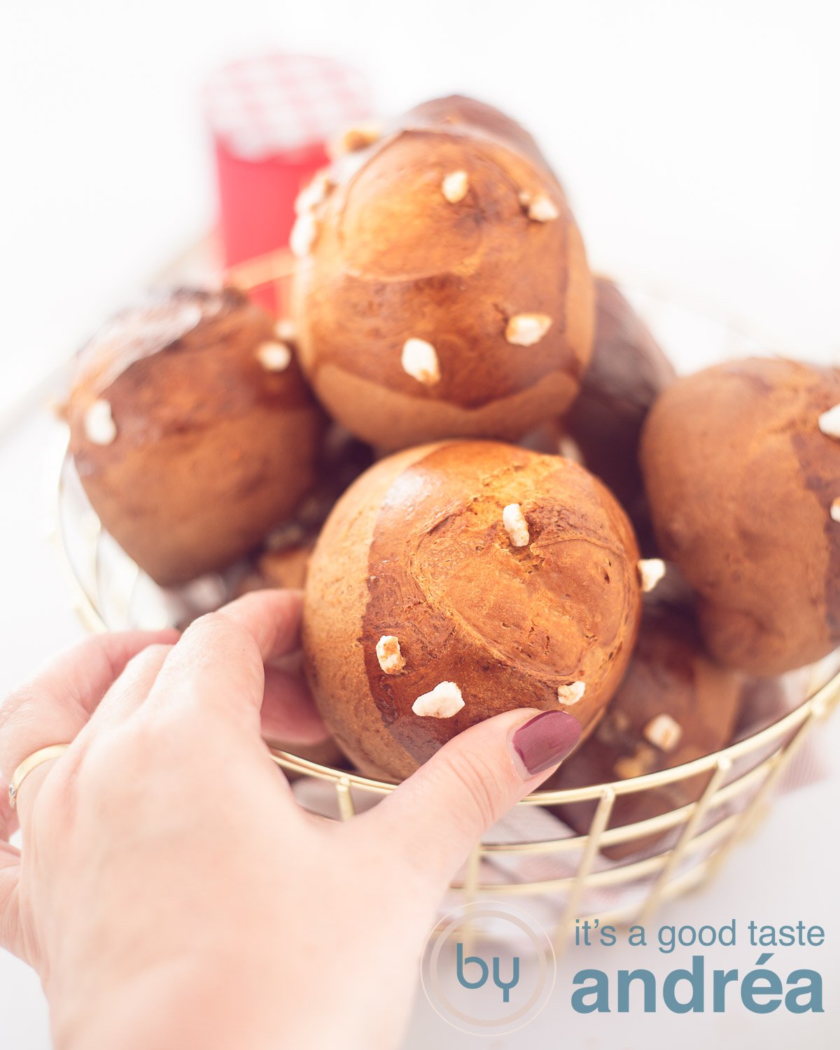 A golden wire basket filled with sugar buns on a white background. A hand grabs a bun.