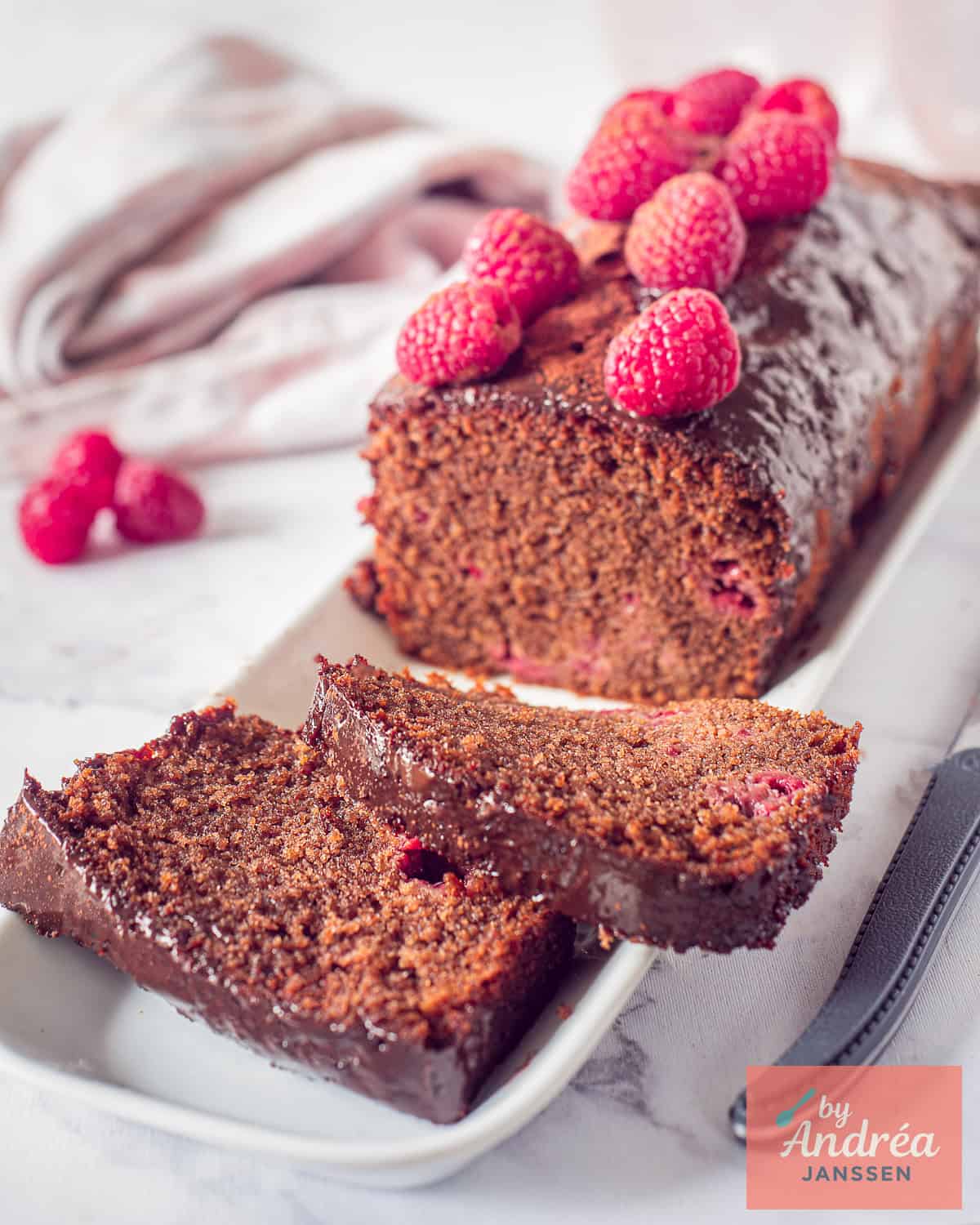 Een deel van een chocolade cake met frambozen en ganache, twee plakjes afgesneden.
