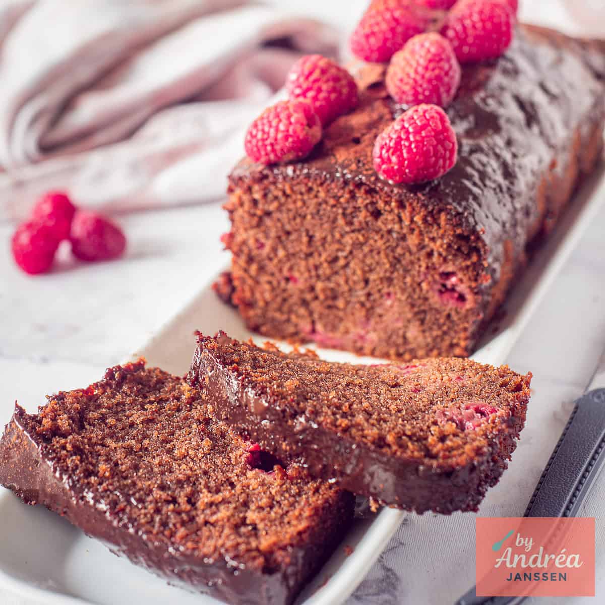A square photo of chocolate cake with raspberries from which two slices have been cut.