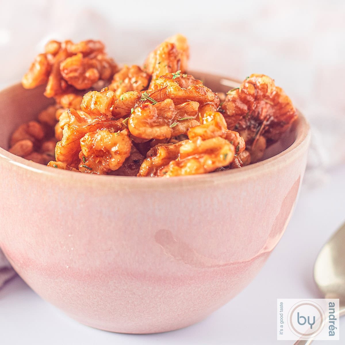 A square photo with a pink bowl of candied walnuts with thyme.