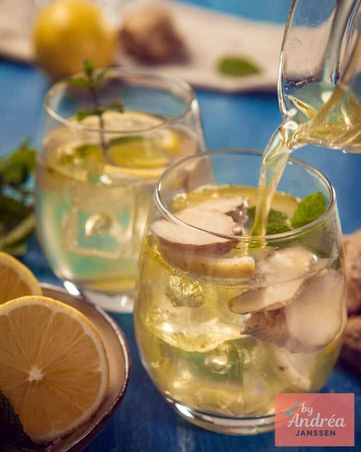 Een kan die gember citroen ijsthee in een glas schenkt