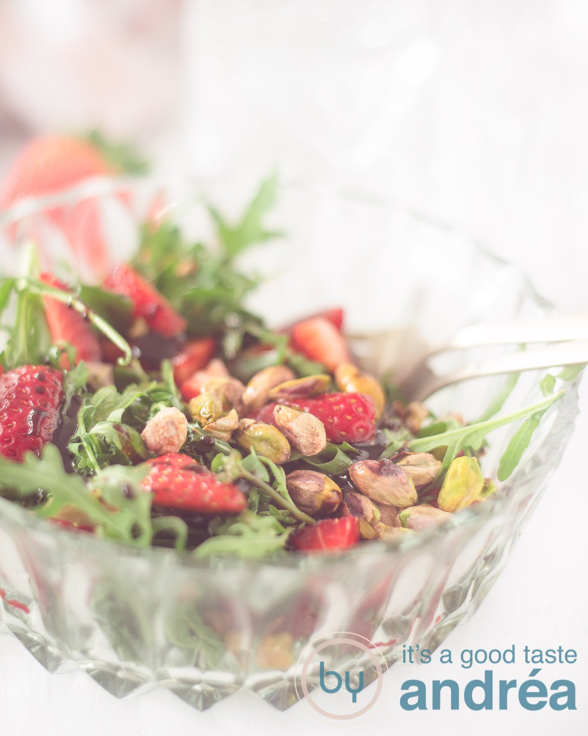 A bowl with strawberry arugula and pistachio salad on a white background