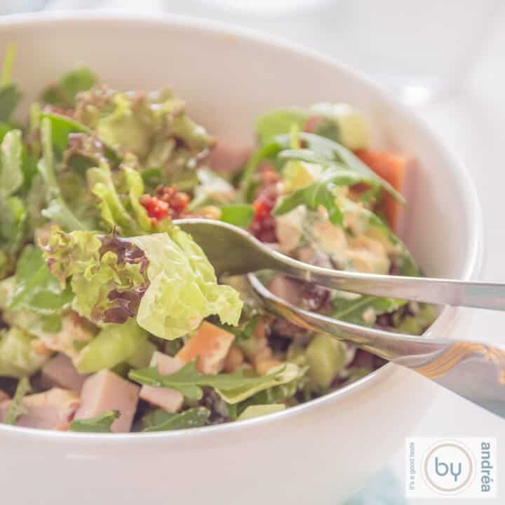 A square photo of a white bowl with green salad, smoked chicken and sun-dried tomatoes.