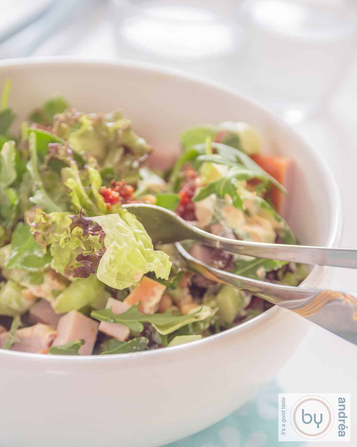 Een deel van een kom met een groene salade met pesto, kip en tomaatjes