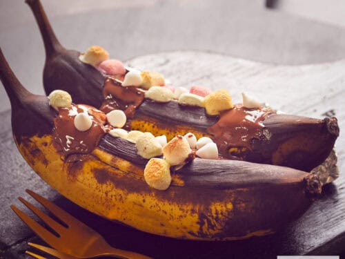 A square photo of two grilled bananas one after the other, flavored with whiskey, melted chocolate and marshmallows