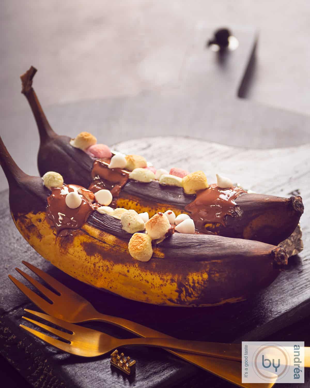 Twee bananen op een houten plank, gegrild en gevuld met whisky, marshmallows en chocola