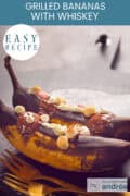 Two bananas on a wooden board with marshmallows, whiskey and chocolate. A text above: easy recipe, grilled bananas with whiskey