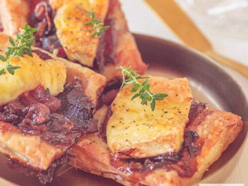 A square photo of puff pastry snacks with red onion, brie and bacon