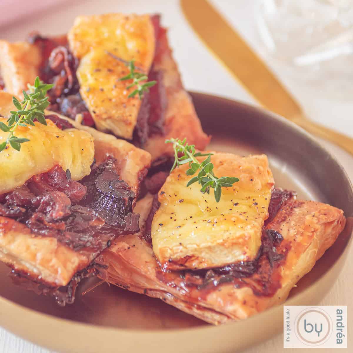 A square photo of puff pastry snacks with red onion, brie and bacon