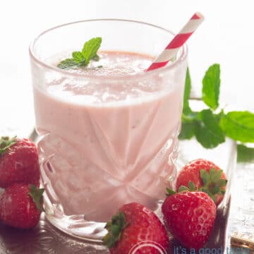 A glass with a Strawberry yogurt orange smoothie surrounded with strawberries and mint