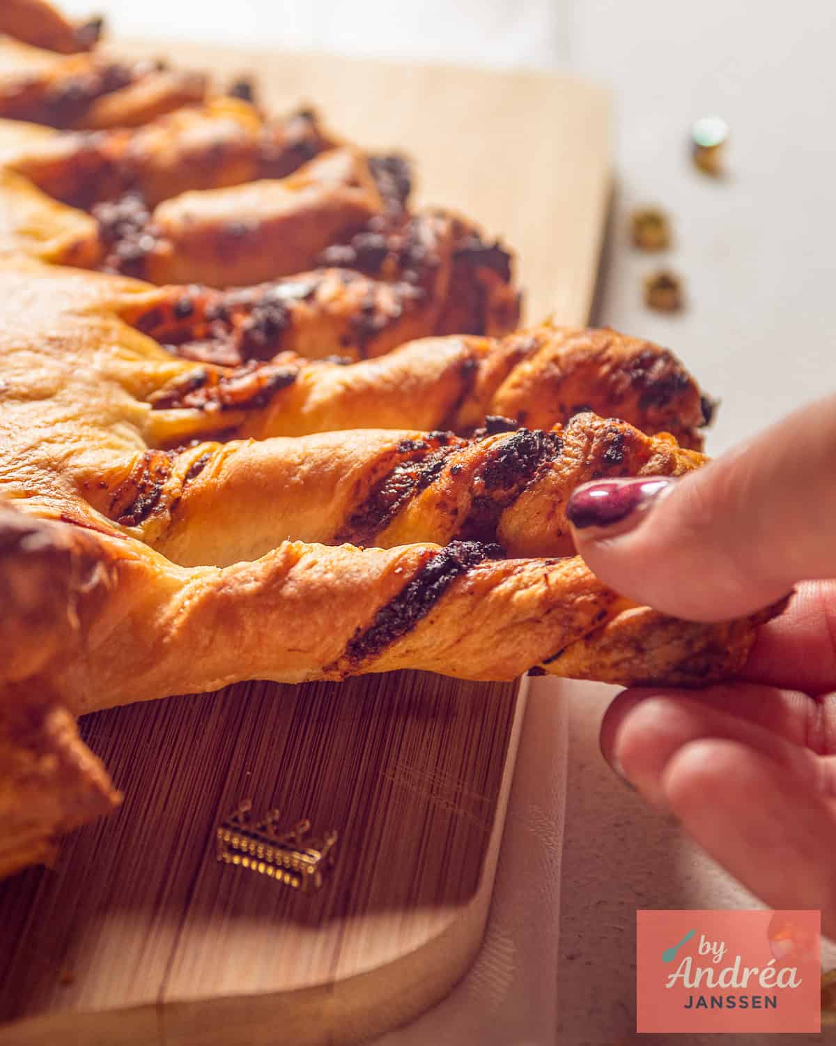A hand breaking off a branch of the puff pastry Christmas tree with pesto.