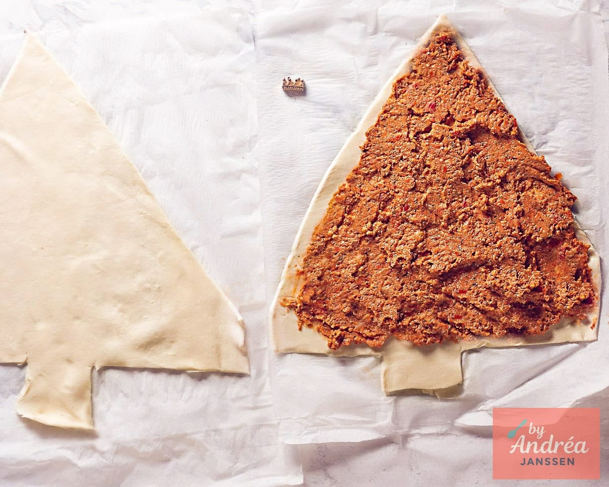 Two pieces of puff pastry in the shape of a Christmas tree, one spread with red pesto.