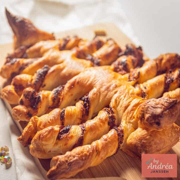 A square photo with a Christmas tree made of puff pastry and red pesto on a piece of baking paper.