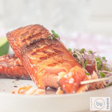 A square photo of a white plate with two pieces of grilled salmon that has been brined.