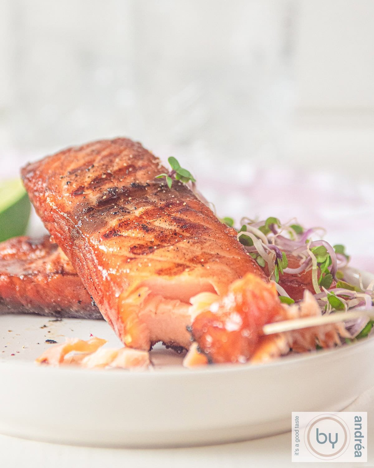 A white plate with two pieces of pickled and grilled salmon, with one piece removed to reveal the inside.