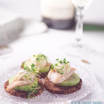 three smoked trout snacks with cucumber and rye bread on a glass plate