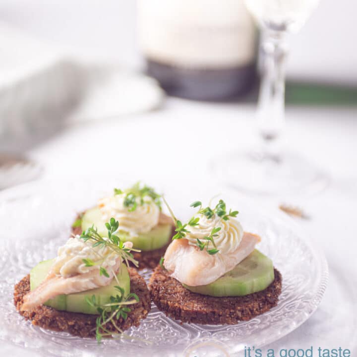 three smoked trout snacks with cucumber and rye bread on a glass plate
