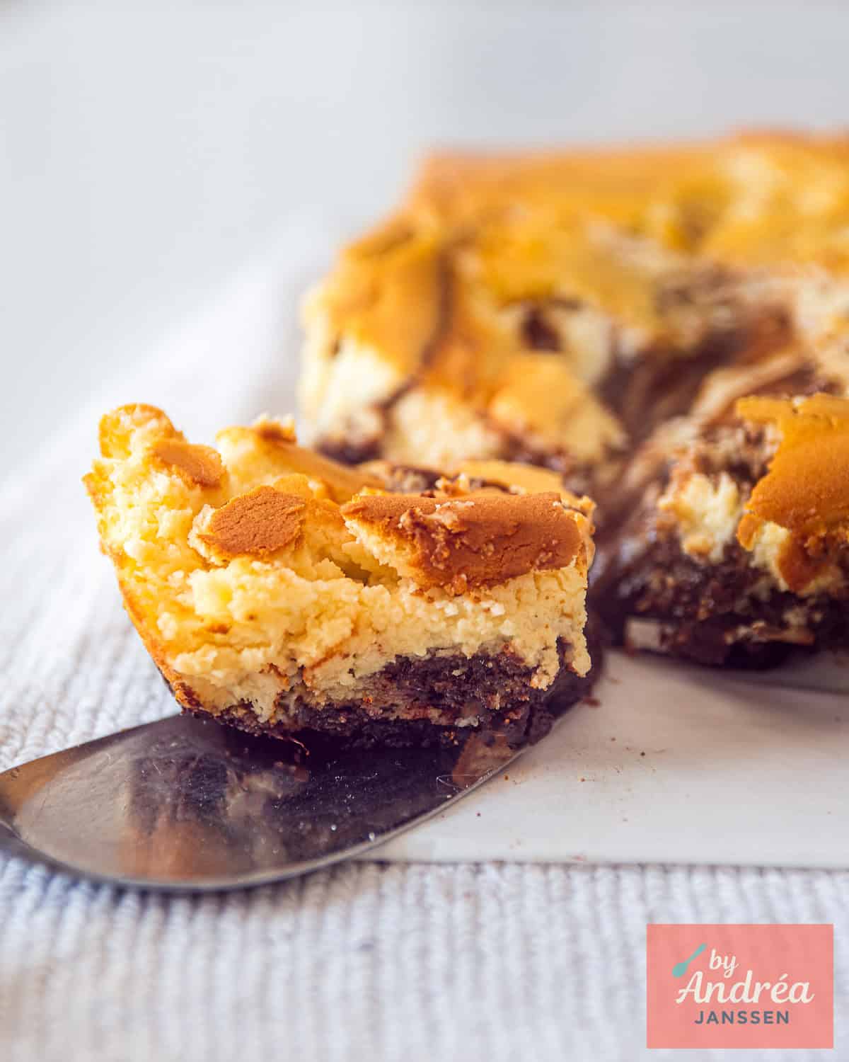 Een deel van een cheesecake brownie. Een vierkant is eraf gesneden en ligt op een taartschep.