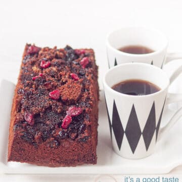 Cake with a caramelized cranberry topping on a white plate and two cups of coffee