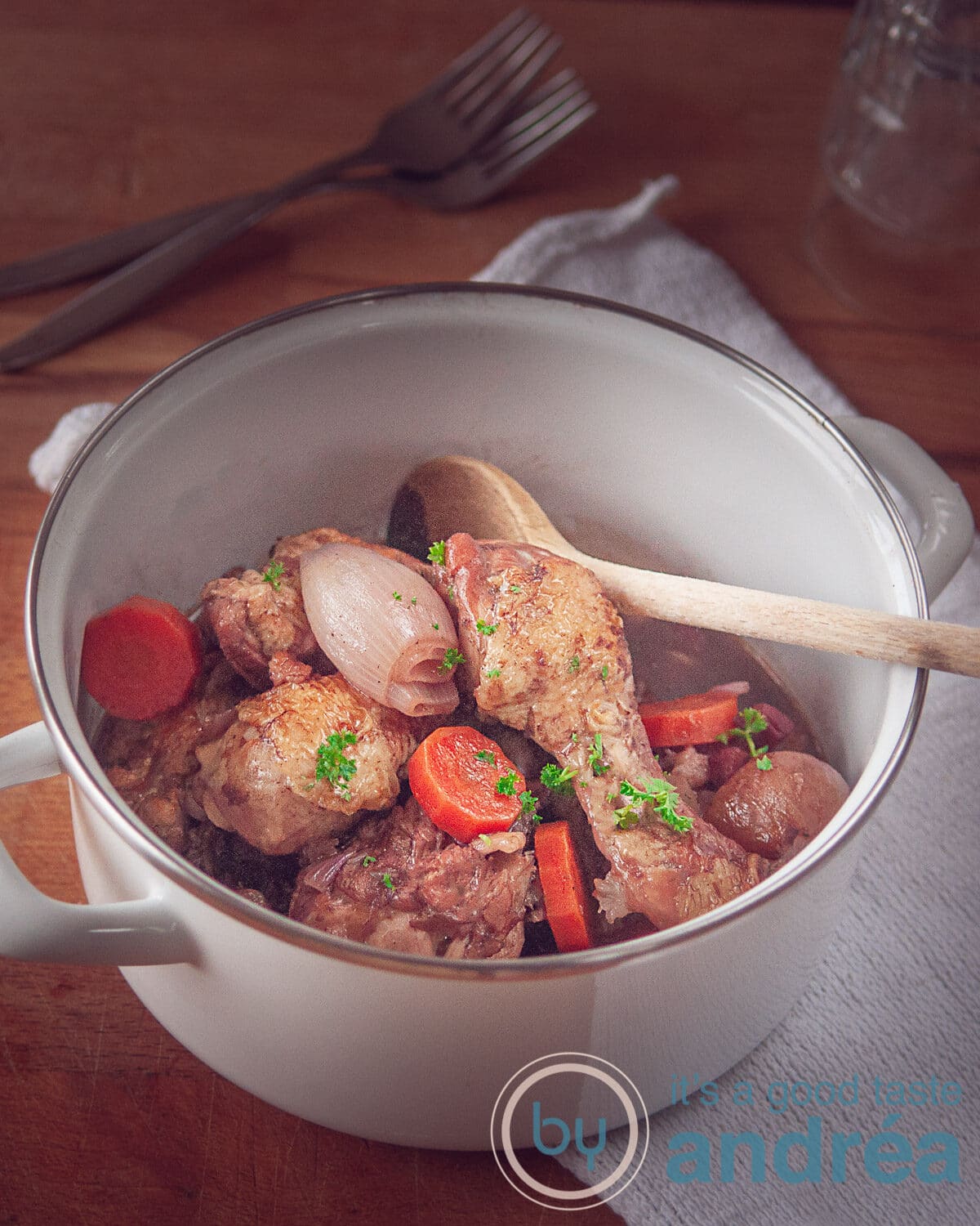 een witte pan met coq au vin op een houten plank