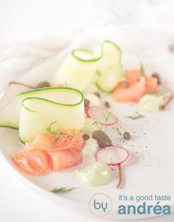 A white plate with cucumber ribbons, smoked salmon and pipings of horseradish and avocado cream