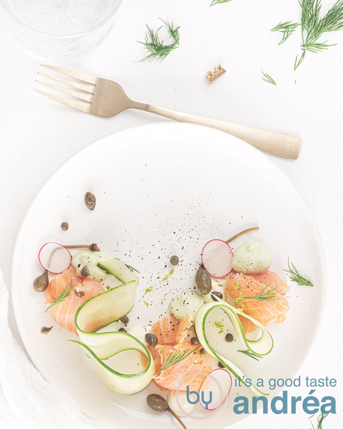 a plate with smoked salmon, cucumber ribbons and two creams a fork and some dill spread around
