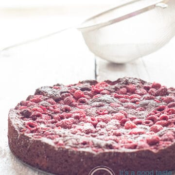 a wooden white plate with a raspberry brownie cake on top. Dusted with confectioners sugar