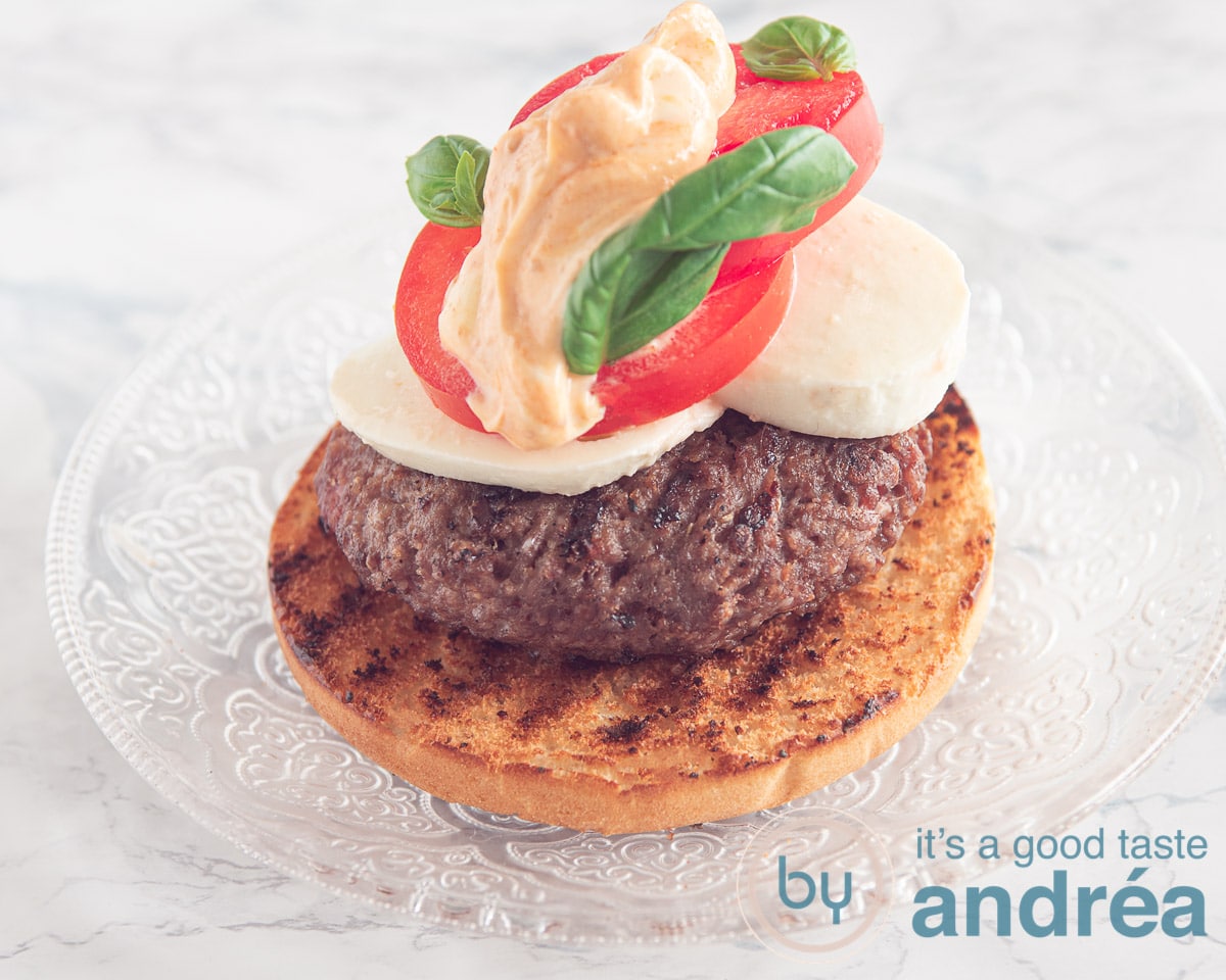 a bun topped with a grilled burger, mozzarella slices, tomato and mayonaise pesto