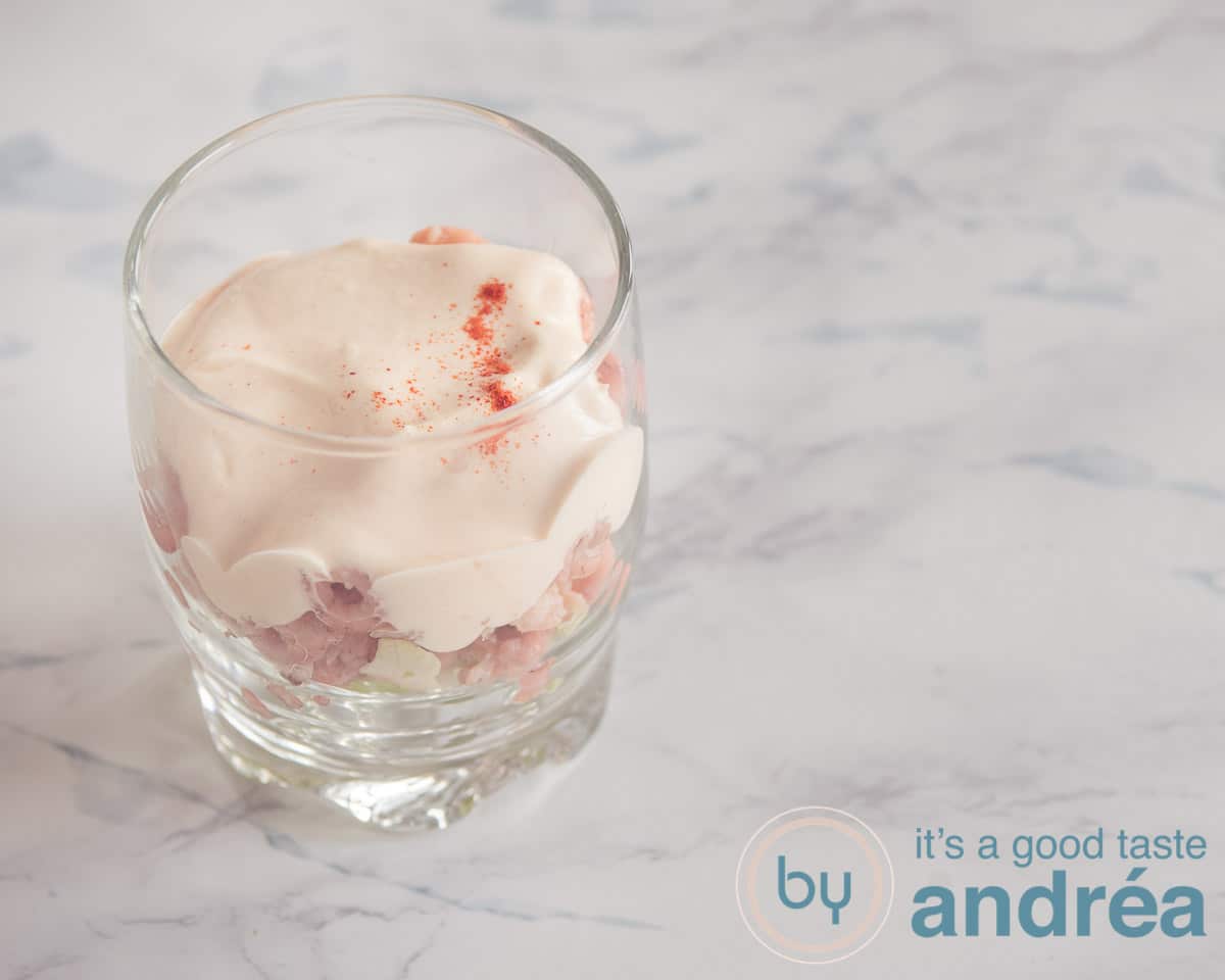 a glass filled with a layer ice berg lettuce, shrimp and cocktail sauce