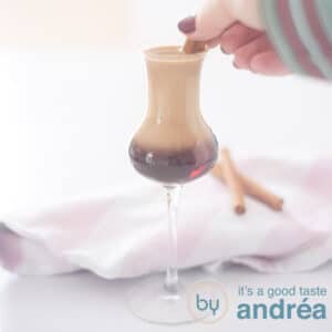 A square photo with a cocktail glass filled with Marakesh and Amarula. A cinnamon stick in it with one hand grabbing it.