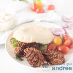 square photo with grilled spicy minced meat in a sandwich with tomatoes around it