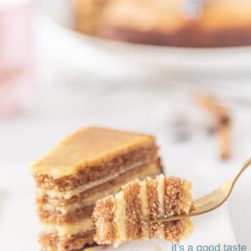 A fork holding a bite of gingerbread. In the background a slice of cake and the whole thousand layers cake