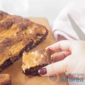 A square photo with a brownie with a piece cut off. A cube of caramel brownie is removed from the cutting board.
