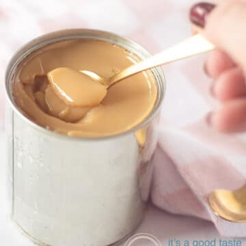 A tin filled with creamy dulce de leche. A golden spoon takes a bit out of the tin. A pink cloth in the background