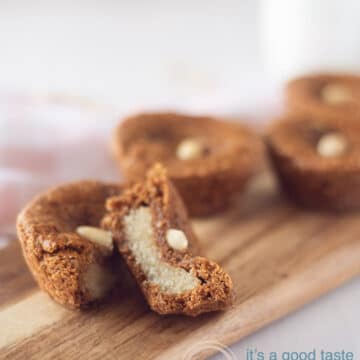 a wooden board with Dutch almond-filled speculaas cookies on a white background. One cookie is sliced in half