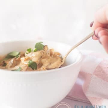 A bowl filled with mushrooms in a cream sauce. A golden spoon and a hand taking out a shovel. A pink and white checkered tea towel on the right