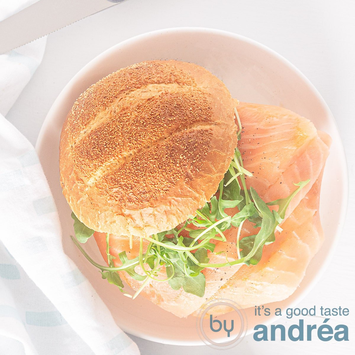 A square shot of a salmon cream cheese sandwich from above on a white plate with a white background.