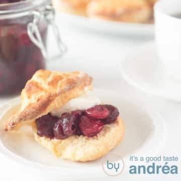 A square photo with a scone filled with clotted cream and cranberry compote. A white background.