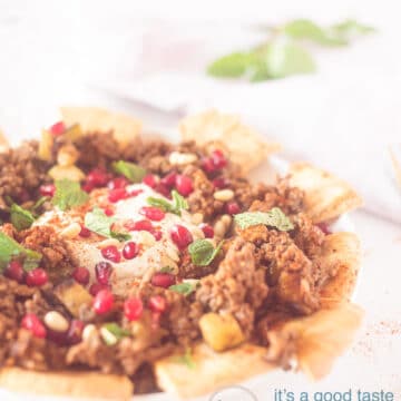 A photo of part of a plate filled with Fatteh, with yogurt dip and a topping of mint and pomegranate seeds. A white background.