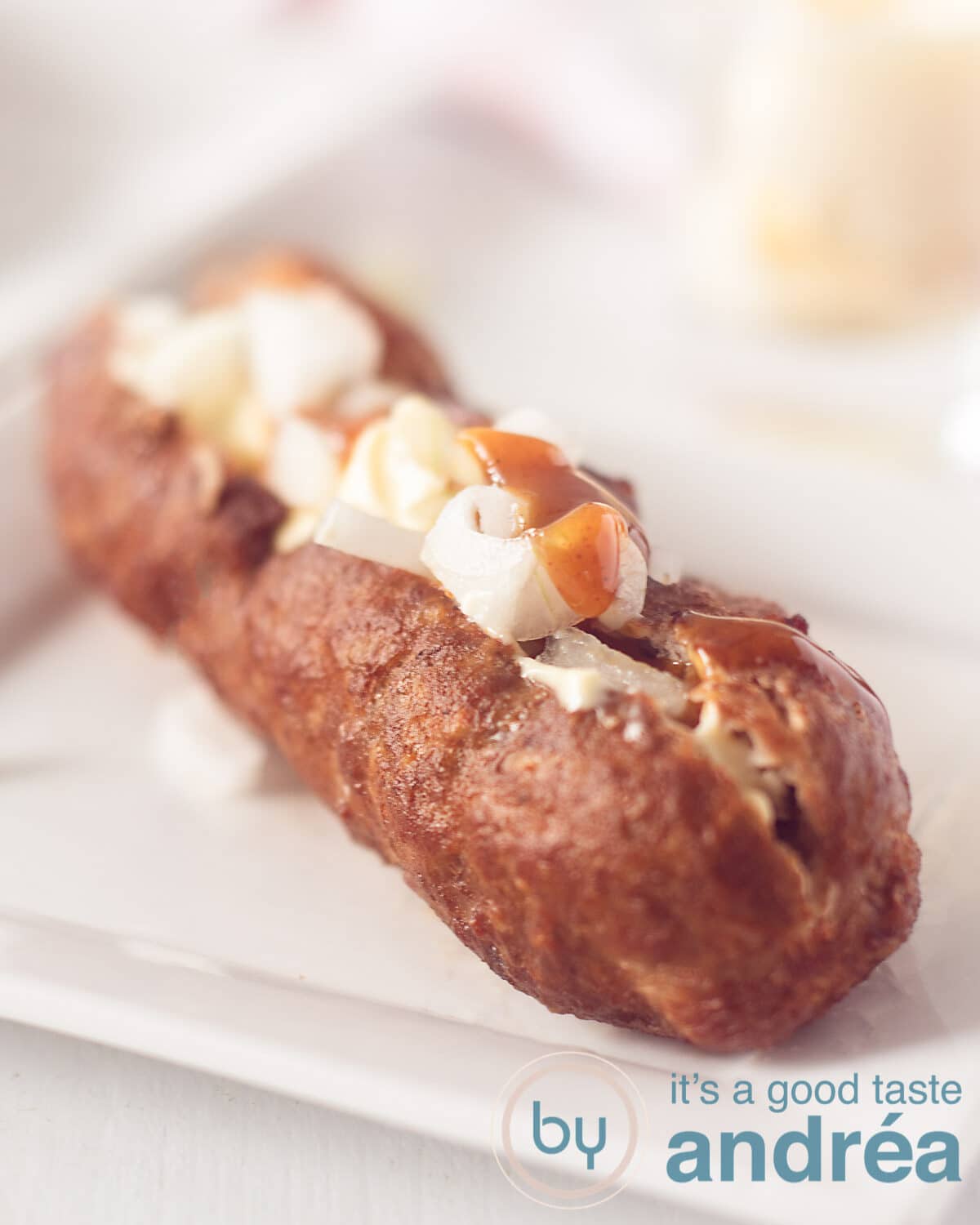A frikandel on a white plate filled with onions curry ketchup and mayonaise on a white background