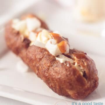 A frikandel on a white plate filled with onions curry ketchup and mayonaise on a white background