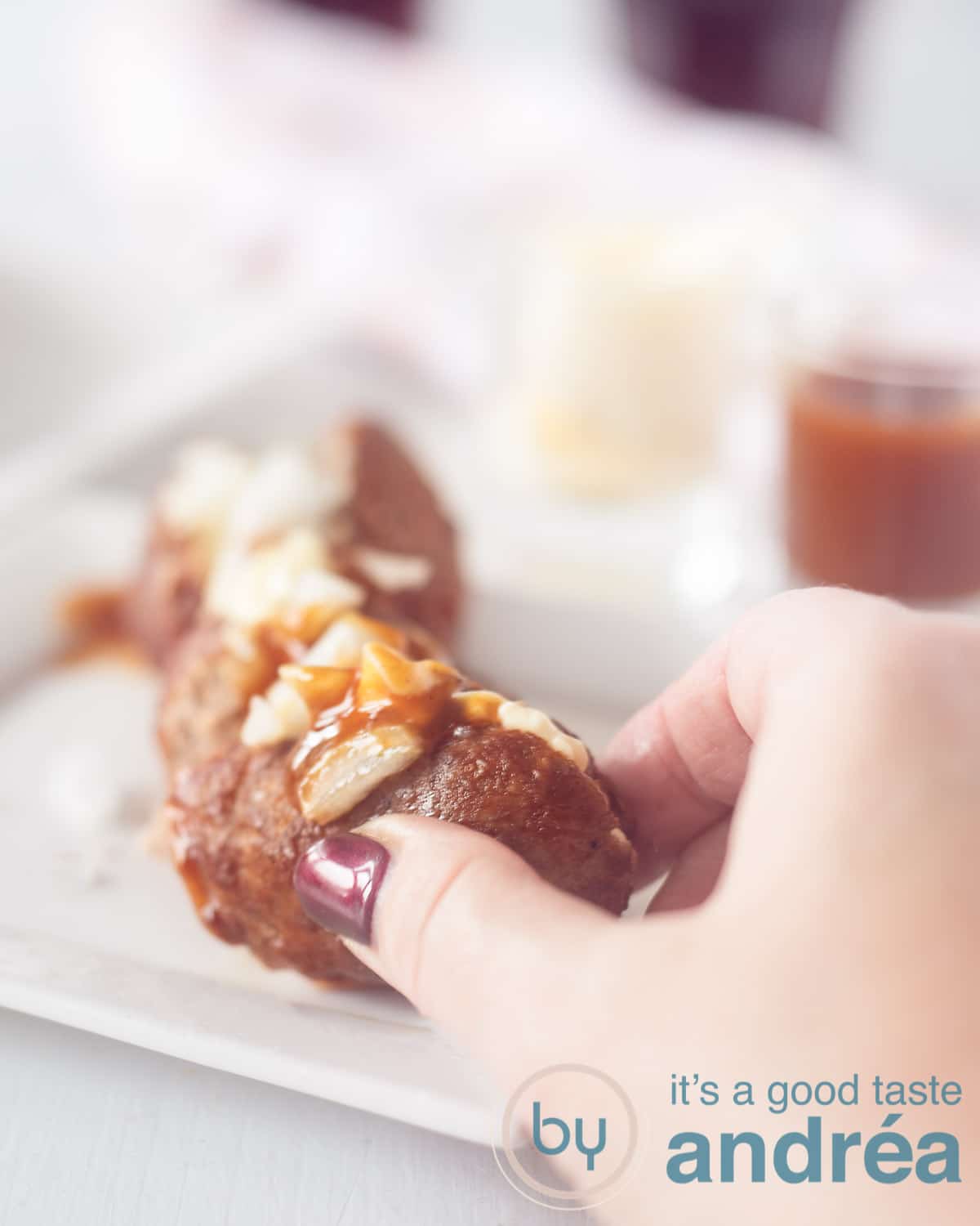 A hand that breaks off a piece of a frikandel speciaal. Some sauces in the background
