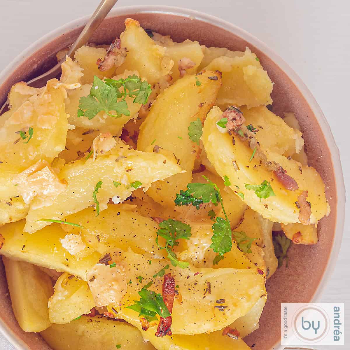 A square photo of roasted garlic potatoes with bacon, herbs and Parmesan cheese