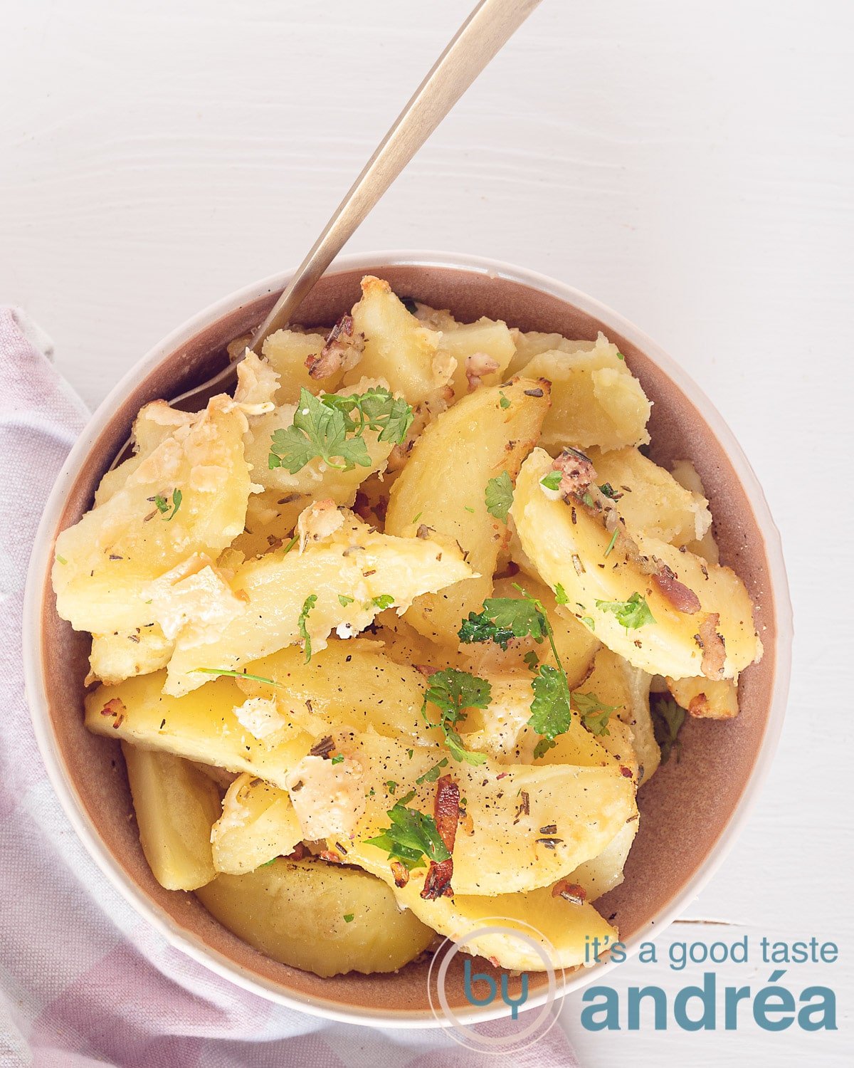 A photo from above of a pink bowl with potatoes, herbs, and garlic
