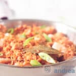 A frying pan with jambalaya, shrimp and spring onions on a white surface. A square photo