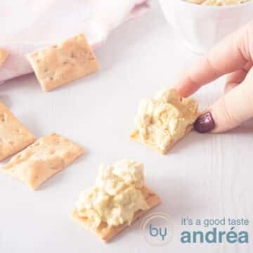 A square picture with two toasts with chicken curry salad. A hand taking one toast.