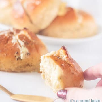 A hand taking a wedge of Korean Garlic Cream cheese bread. Three breads are in the background. A white backdrop
