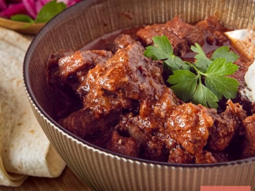 A square photo of Mexican stew in a bowl, with wraps and garnish.